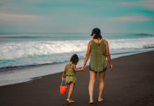 Una madre y su hija pasean de la mano por la arena de la playa.