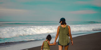 Una madre y su hija pasean de la mano por la arena de la playa.