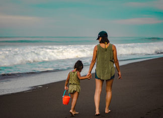 Una madre y su hija pasean de la mano por la arena de la playa.