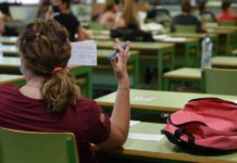 Un aula con alumnos realizando las pruebas de Selectividad (PAU) en mesas y sillas verdes.