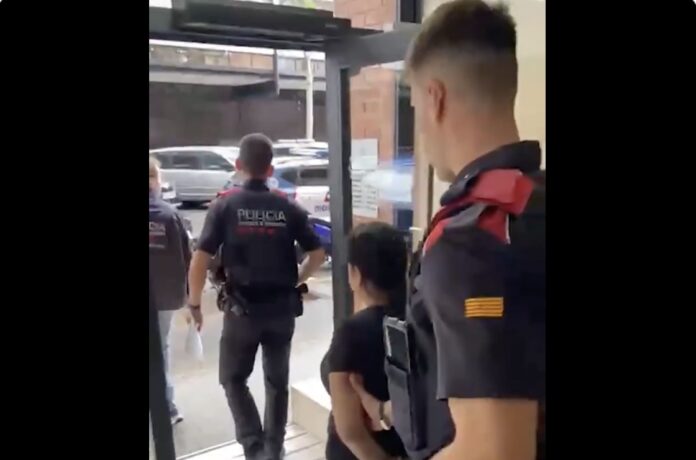 Momento en el que una de las detenidas abandona el portal del domicilio acompañada por los Mossos.