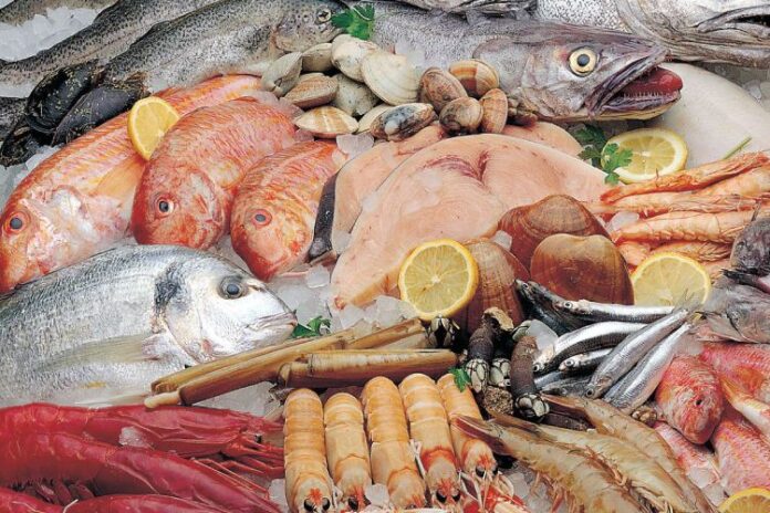 Variedad de pescados y mariscos frescos sobre hielo, con rodajas de limón.