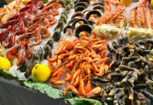 Mostrador de pescadería con diversos tipos de marisco fresco, incluyendo cangrejos y otros decápodos, bajo el hielo.