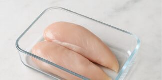 Pechugas de pollo crudas colocadas en un recipiente de vidrio sobre una encimera de mármol.