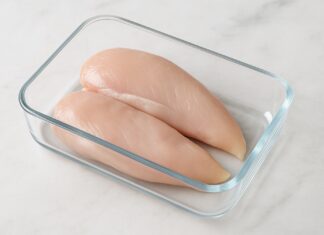 Pechugas de pollo crudas colocadas en un recipiente de vidrio sobre una encimera de mármol.