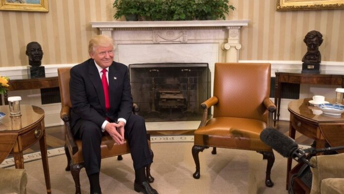 El presidente Donald Trump sentado en el Despacho Oval al lado de una silla vacía.