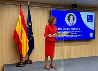 La ministra de Hacienda, María Jesús Montero, en una rueda de prensa en Bruselas, delante de las banderas de España y la UE y de una pantalla con sus datos.