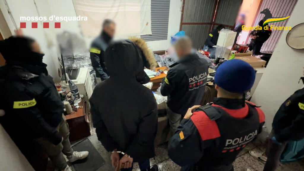 Agentes de los Mossos d’Esquadra y la Guardia di Finanza custodian a un detenido esposado durante un registro en una vivienda en el marco de una operación contra el narcotráfico.