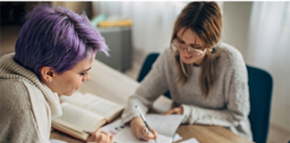 Dos mujeres, una con el pelo lila y otra morena, revisan documentos en una mesa.