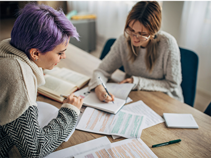 Dos mujeres, una con el pelo lila y otra morena, revisan documentos en una mesa.