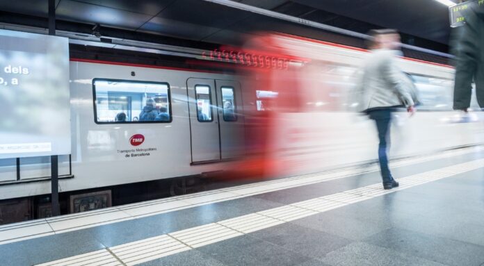 Vagón del metro de Barcelona con el logotipo de TMB circulando por una estación con pasajeros en el andén durante el Mobile World Congress.