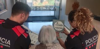 Dos agentes de los Mossos d'Esquadra muestran un folleto con consejos de seguridad a una mujer de avanzada edad para prevenir estafas.