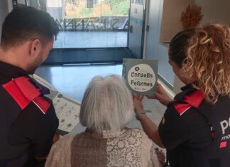 Dos agentes de los Mossos d'Esquadra muestran un folleto con consejos de seguridad a una mujer de avanzada edad para prevenir estafas.