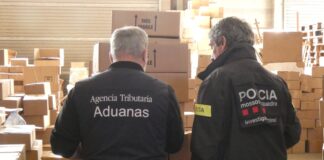 Un agente de los Mossos d’Esquadra y otro de Vigilancia Aduanera observan de espaldas miles de cajas de perfumes falsificados en una nave de La Selva.