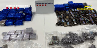 Paquetes de hachís de diversos formatos e insignias de los Mossos d’Esquadra y la Guardia di Finanza sobre una mesa tras una operación policial.