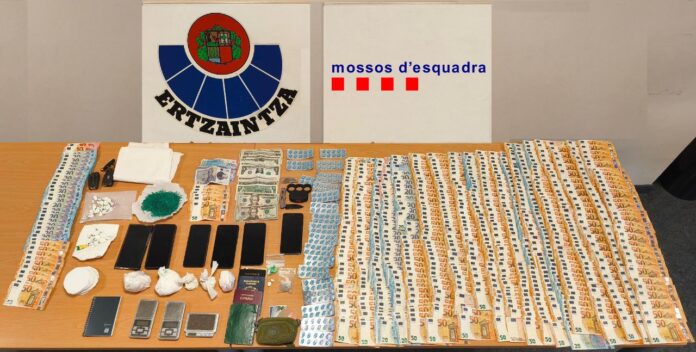Mesa con fajos de billetes, envoltorios de droga, teléfonos móviles y básculas de precisión incautados en una operación policial.