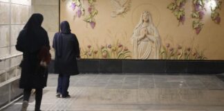 Mural de la Virgen María en una estación de metro de Teherán, Irán, mientras dos mujeres caminan frente a ella.
