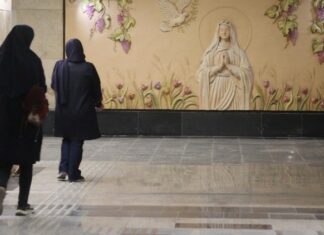 Mural de la Virgen María en una estación de metro de Teherán, Irán, mientras dos mujeres caminan frente a ella.
