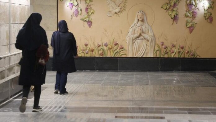 Mural de la Virgen María en una estación de metro de Teherán, Irán, mientras dos mujeres caminan frente a ella.