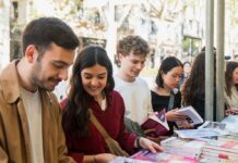Jóvenes sonrientes hojeando libros en un puesto exterior en Barcelona.