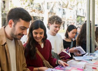 Jóvenes sonrientes hojeando libros en un puesto exterior en Barcelona.