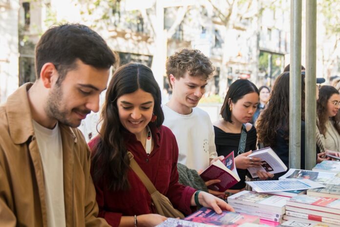 Jóvenes sonrientes hojeando libros en un puesto exterior en Barcelona.