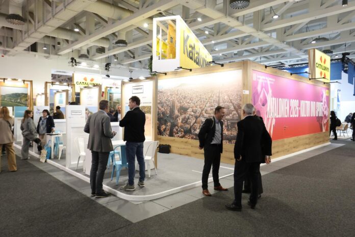 Vista general del stand de Cataluña en la Feria Internacional de Turisme de Berlín (ITB), con una gran fotografía aérea de Barcelona y profesionales del sector conversando.