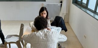 Imagen de una sesión de tutoría individual en un aula, con una orientadora laboral atendiendo a un joven de espaldas que está escribiendo en unos documentos.