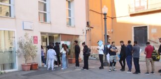 Larga cola de personas extranjeras esperando en la puerta de una oficina de servicios municipales en un ayuntamiento para tramitar papeles.