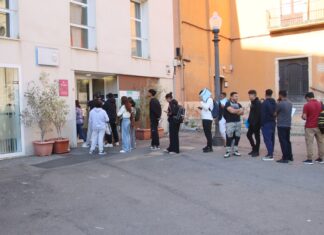 Larga cola de personas extranjeras esperando en la puerta de una oficina de servicios municipales en un ayuntamiento para tramitar papeles.