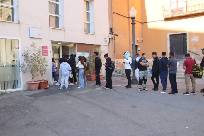 Larga cola de personas extranjeras esperando en la puerta de una oficina de servicios municipales en un ayuntamiento para tramitar papeles.
