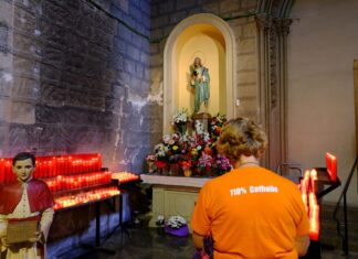 Interior de la iglesia de Sant Jaume en Barcelona con velas encendidas y una persona rezando