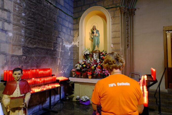Interior de la iglesia de Sant Jaume en Barcelona con velas encendidas y una persona rezando