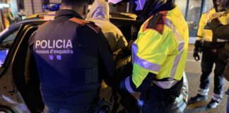 Primer plano de dos agentes de los Mossos d’Esquadra, uno de paisano con chaleco y otro con chaqueta reflectante, deteniendo a un hombre con sudadera con capucha de noche.