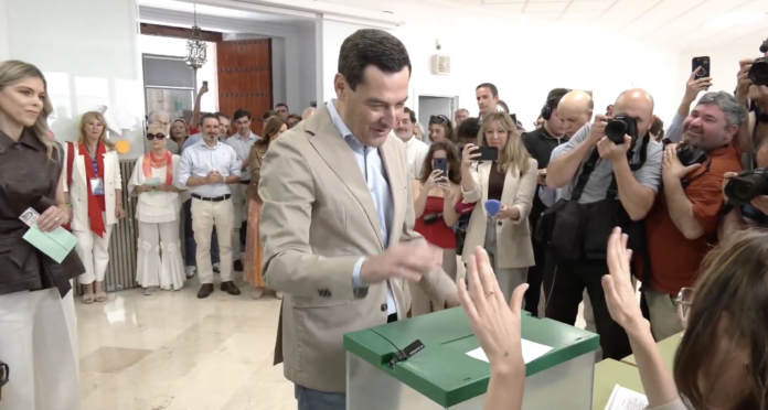 Juanma Moreno Bonilla votando en las elecciones andaluzas de 2026 rodeado de periodistas y fotógrafos.