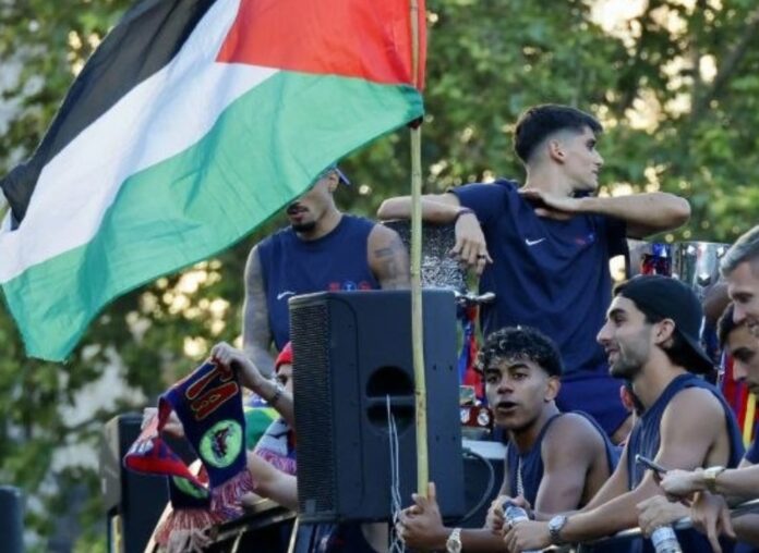 Lamine Yamal junto a una bandera palestina durante la rúa del FC Barcelona por las calles de Barcelona.