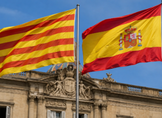 Banderas de Cataluña y España ondeando juntas frente a un edificio institucional.