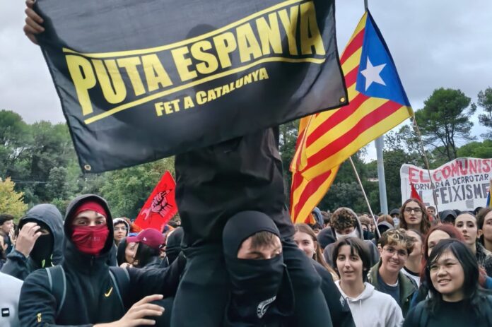 Manifestantes encapuchados con una estelada y pancartas independentistas y comunistas durante las protestas contra Vito Quiles en la UAB.
